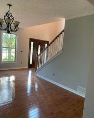 Entryway with hardwood floors, staircase, chandelier, and a brown front door.