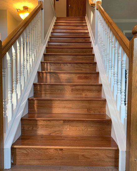 Wooden staircase with white railings, ascending upwards, leading to a closed door.