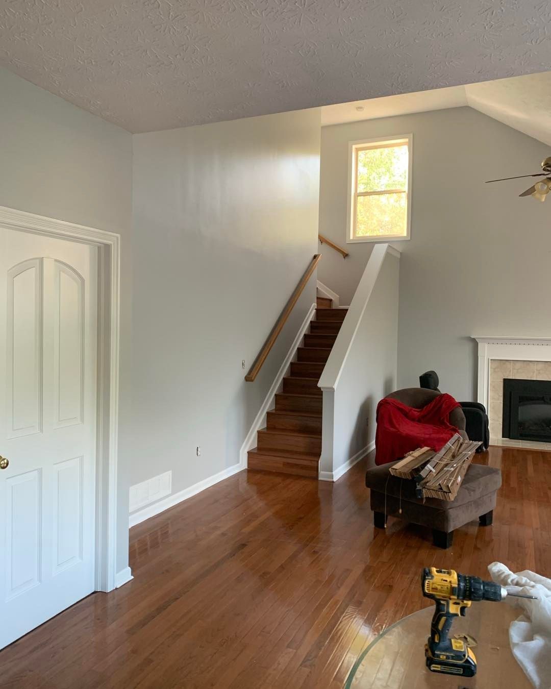 A light blue painted living room with wooden floors, stairs, and a white door.