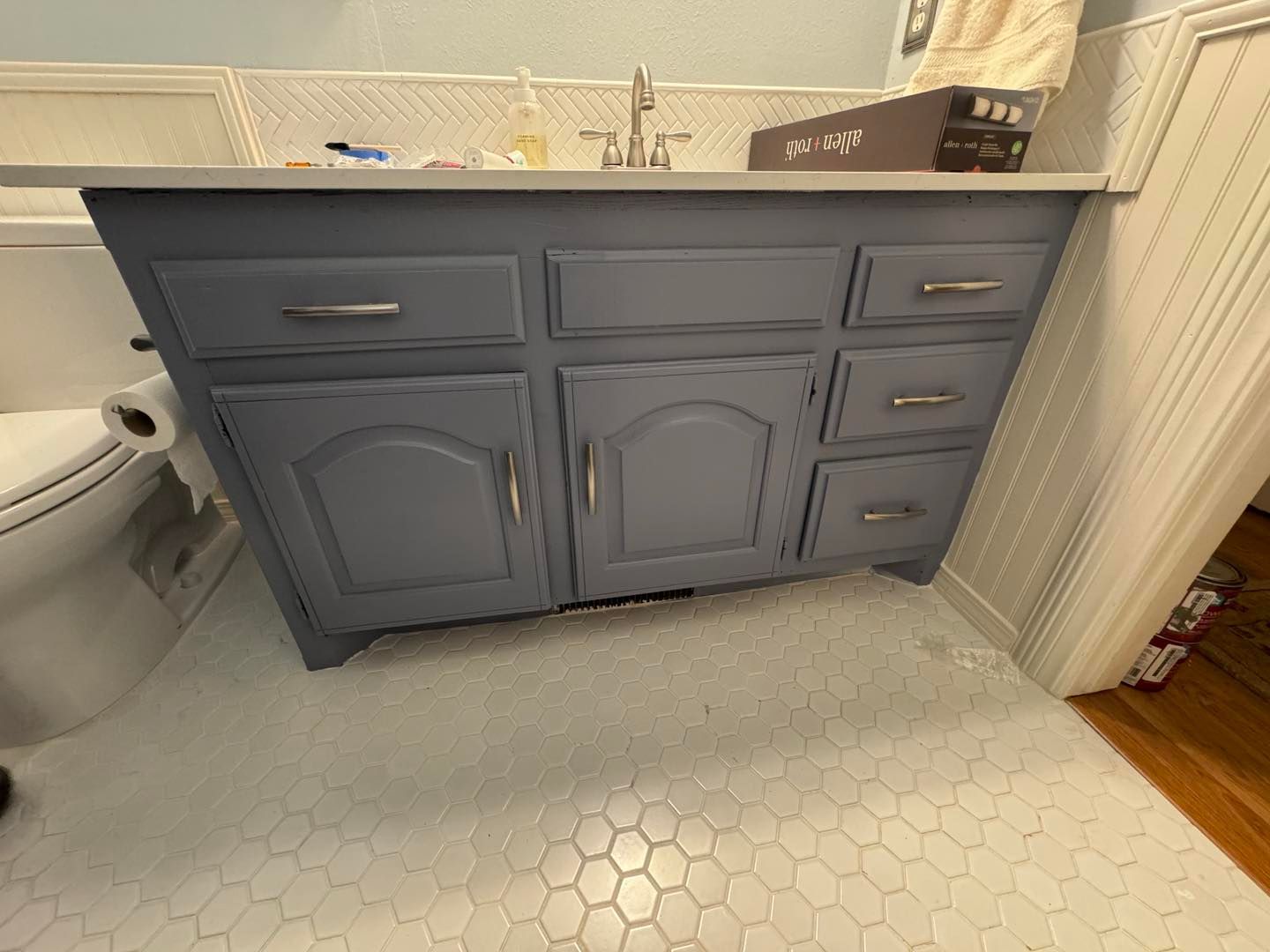 Bathroom vanity with gray cabinets, white countertop, and hexagon tile floor.