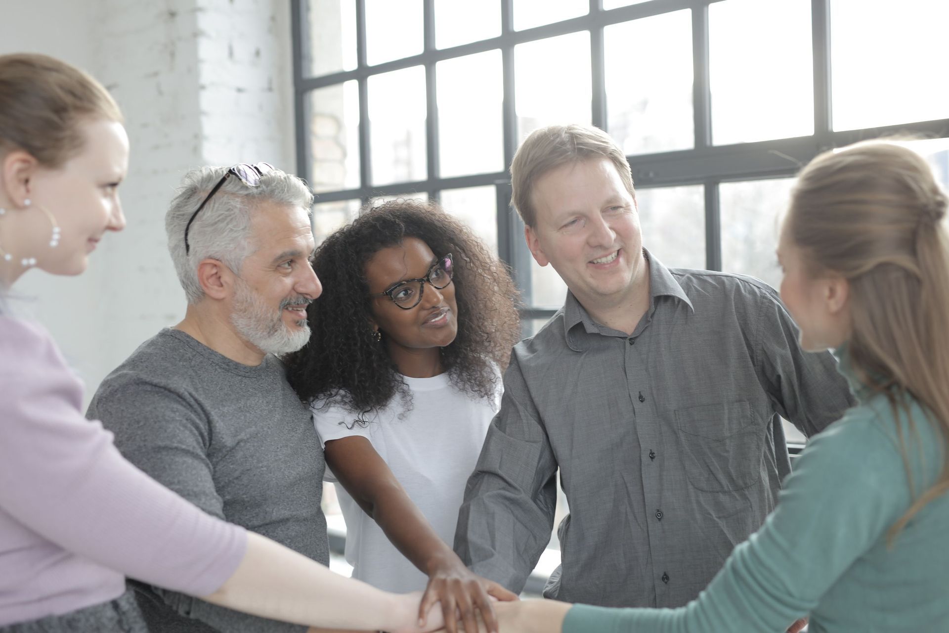 Team smiling in a circle, stacking hands in a bright office meeting room
