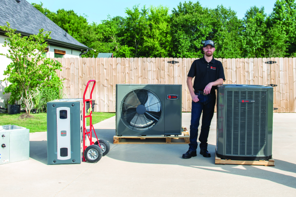 A man is standing next to three air conditioners in a driveway.