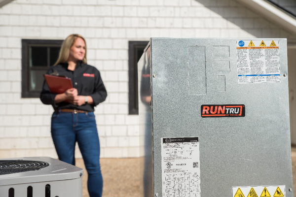 A woman is standing in front of a run tru air conditioner