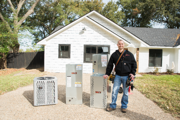 A man is standing in front of a house with air conditioners.