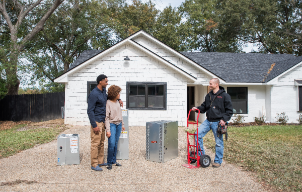 A man and a woman are standing in front of a white house talking to a plumber.