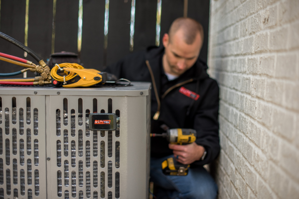 Comfort Control technician is using a drill to fix an air conditioner.