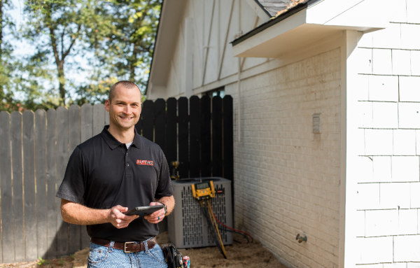 Comfort Control technician is standing in front of a house holding a tablet.