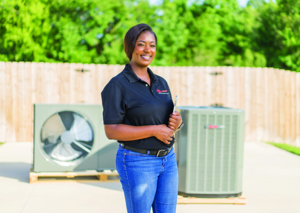 A woman is standing in front of an air conditioner holding a clipboard.