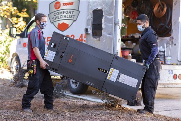 Comfort Control technicians are carrying a large black box in front of a comfort specialist van.