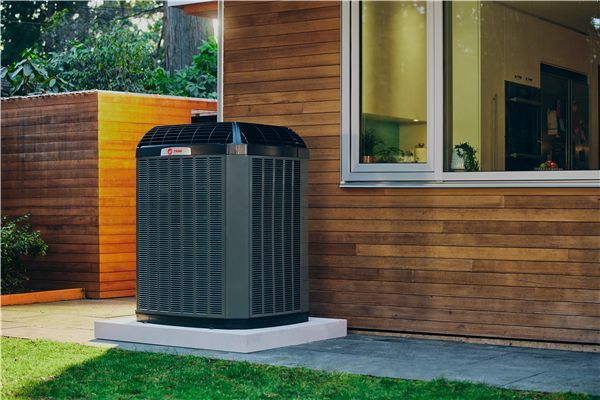 An air conditioner is sitting outside of a house next to a window.