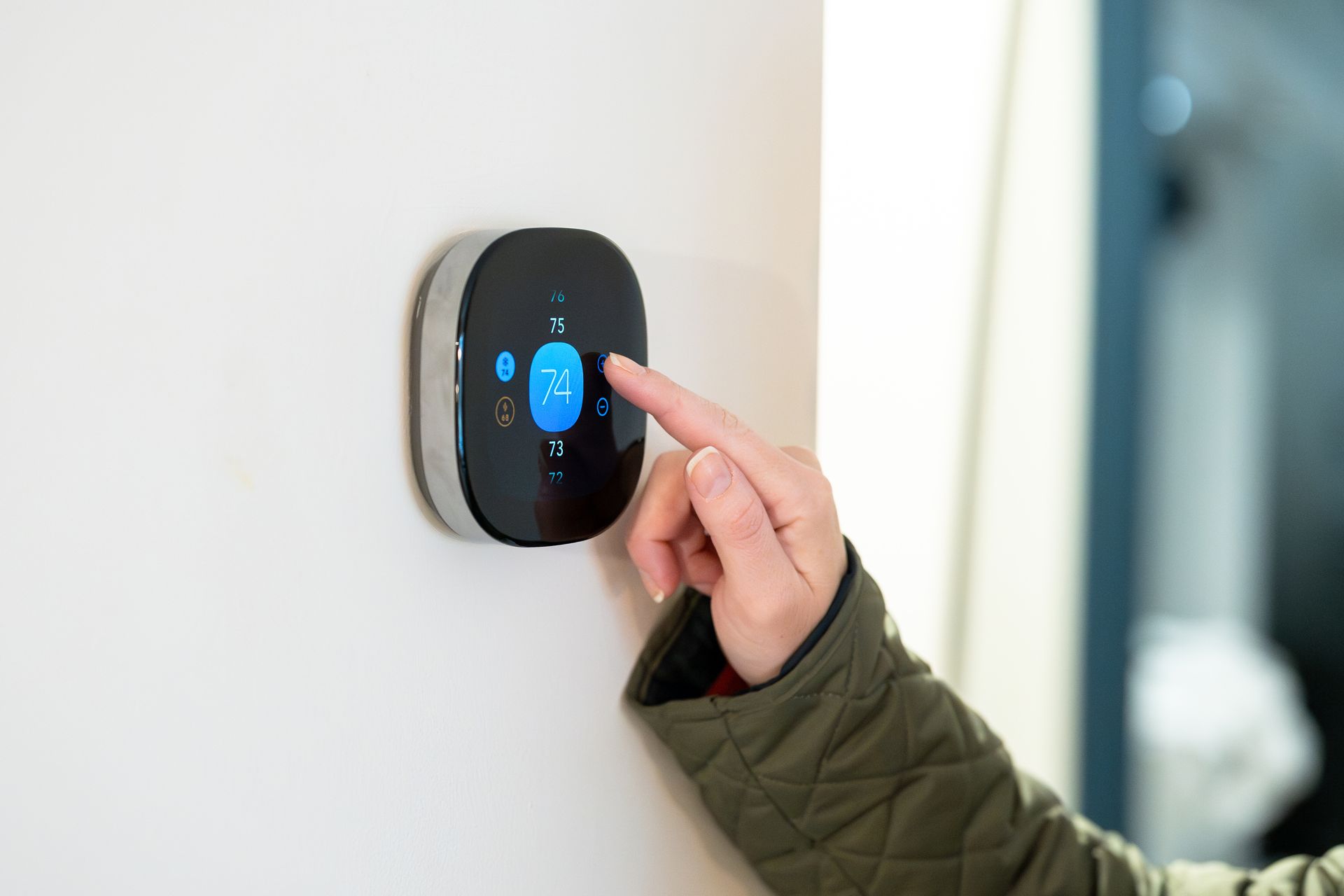 Homeowner adjust WiFi-enabled smart thermostat to improve HVAC energy efficiency in Gluckstadt home.