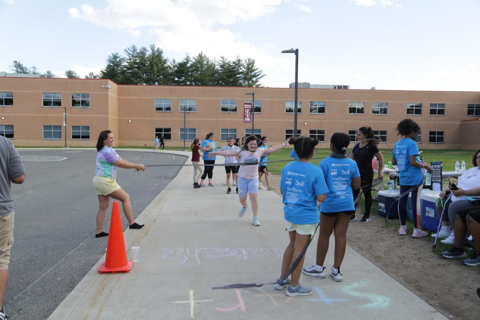 A group of people are standing on a sidewalk wearing blue shirts that say 