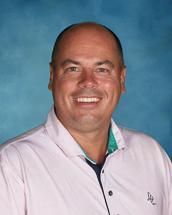 A man in a pink shirt is smiling in front of a blue background.
