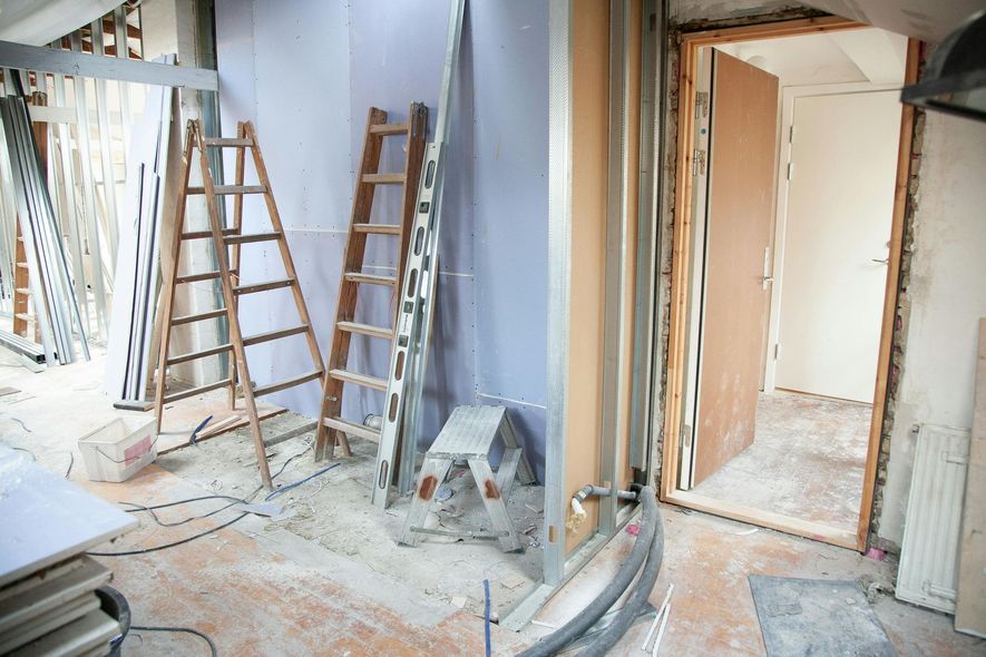 Interior room under construction, with ladders, framing, debris, and open doorway.