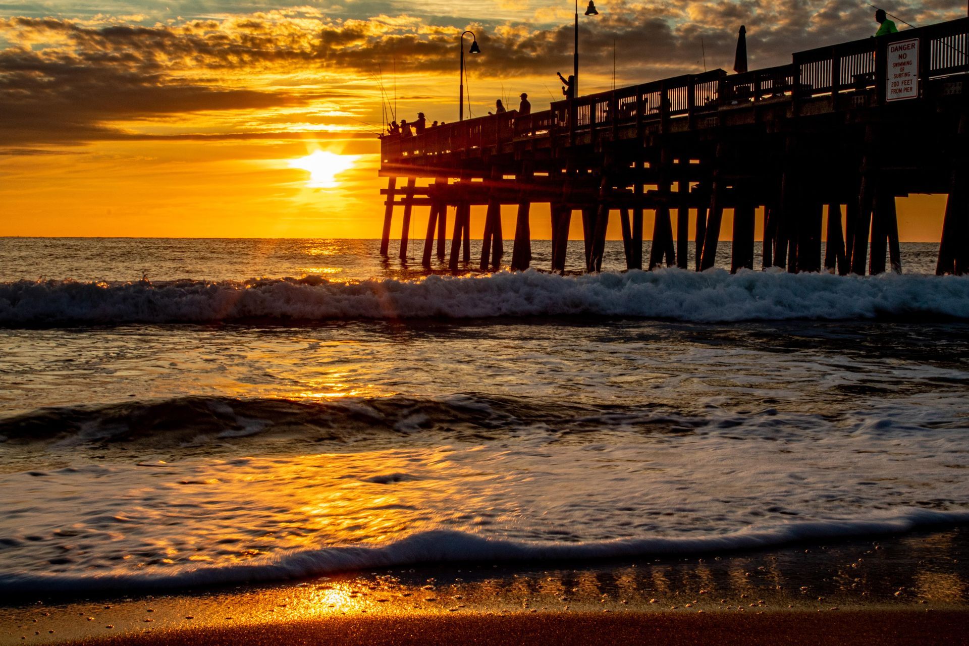 The sun is setting over the ocean and a pier is in the foreground.