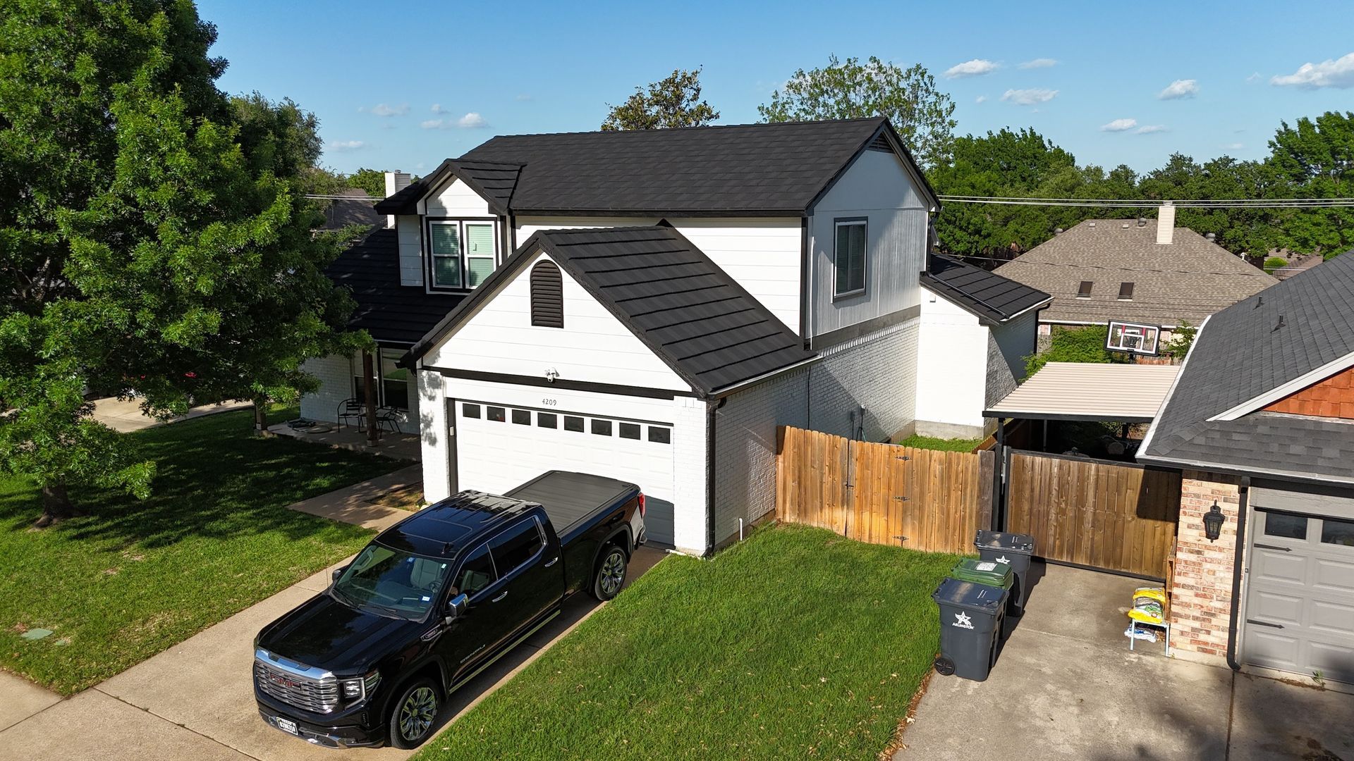 Two-story white house with black roof, garage, and black truck parked in front.