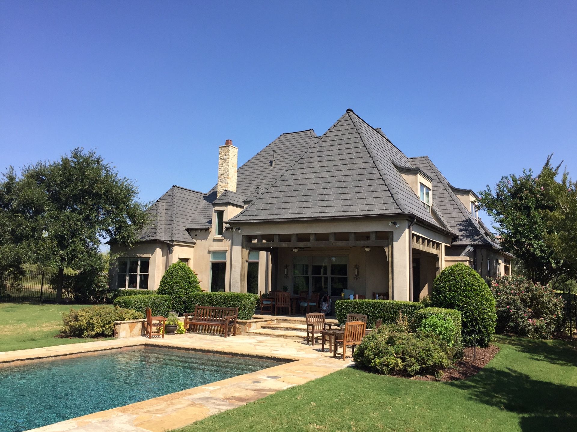 A large house with a gray roof and a swimming pool in the backyard on a sunny day.