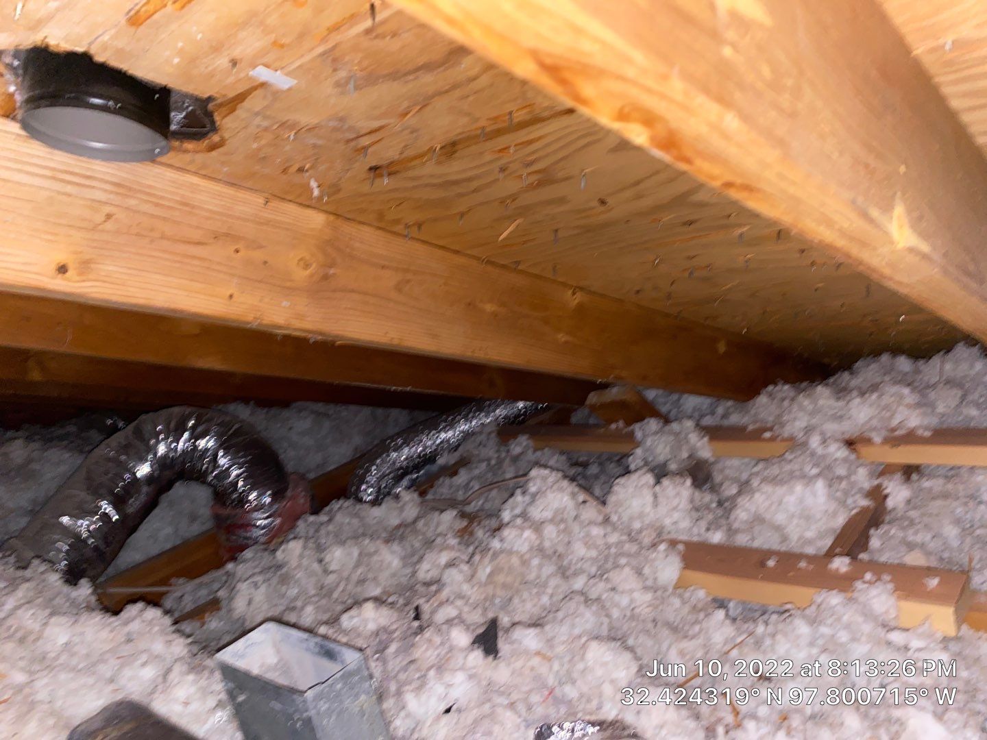 Attic view with insulation, ductwork, and wooden beams.