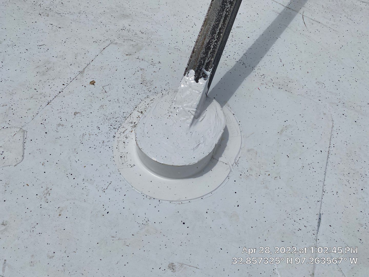 Close-up view of a white, circular roof penetration sealed with white sealant, a tool positioned above it.