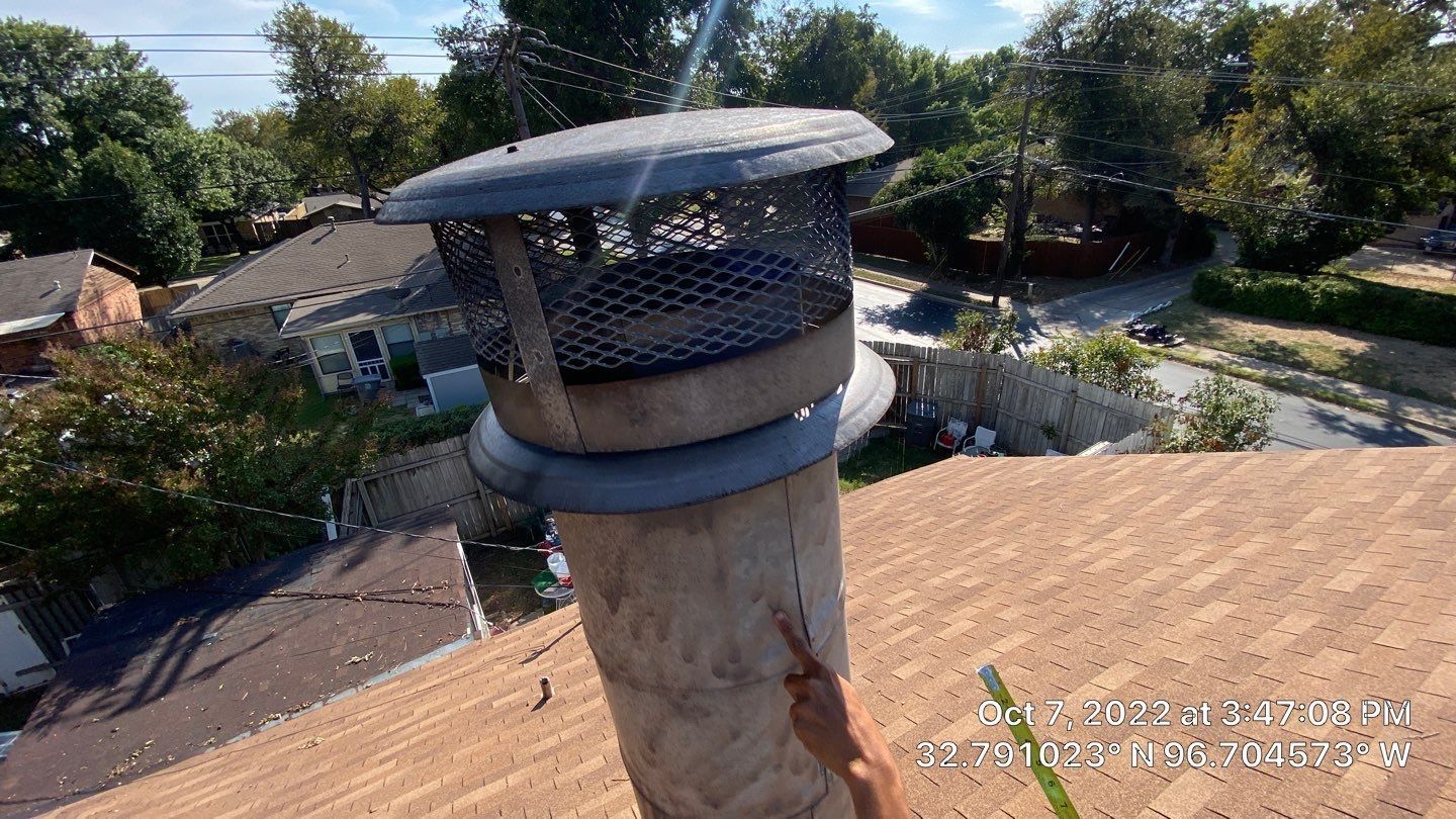 Chimney with mesh cap on rooftop with trees in the background.