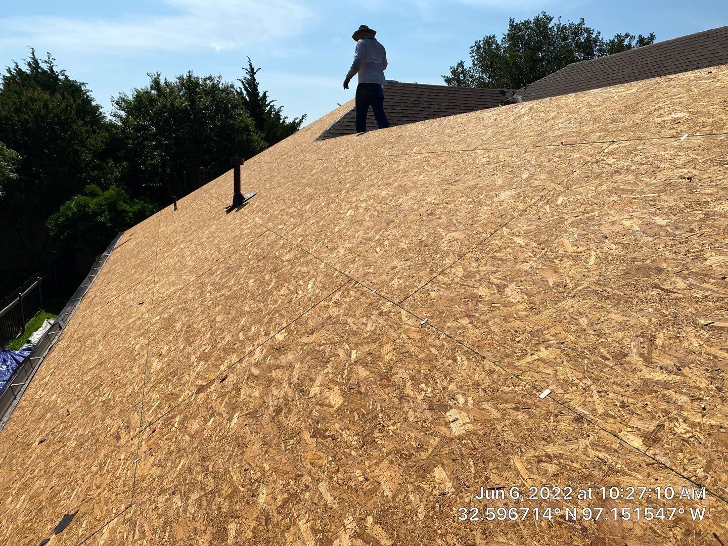 Person on a newly sheathed roof with OSB. The sky is blue and trees are in the background.