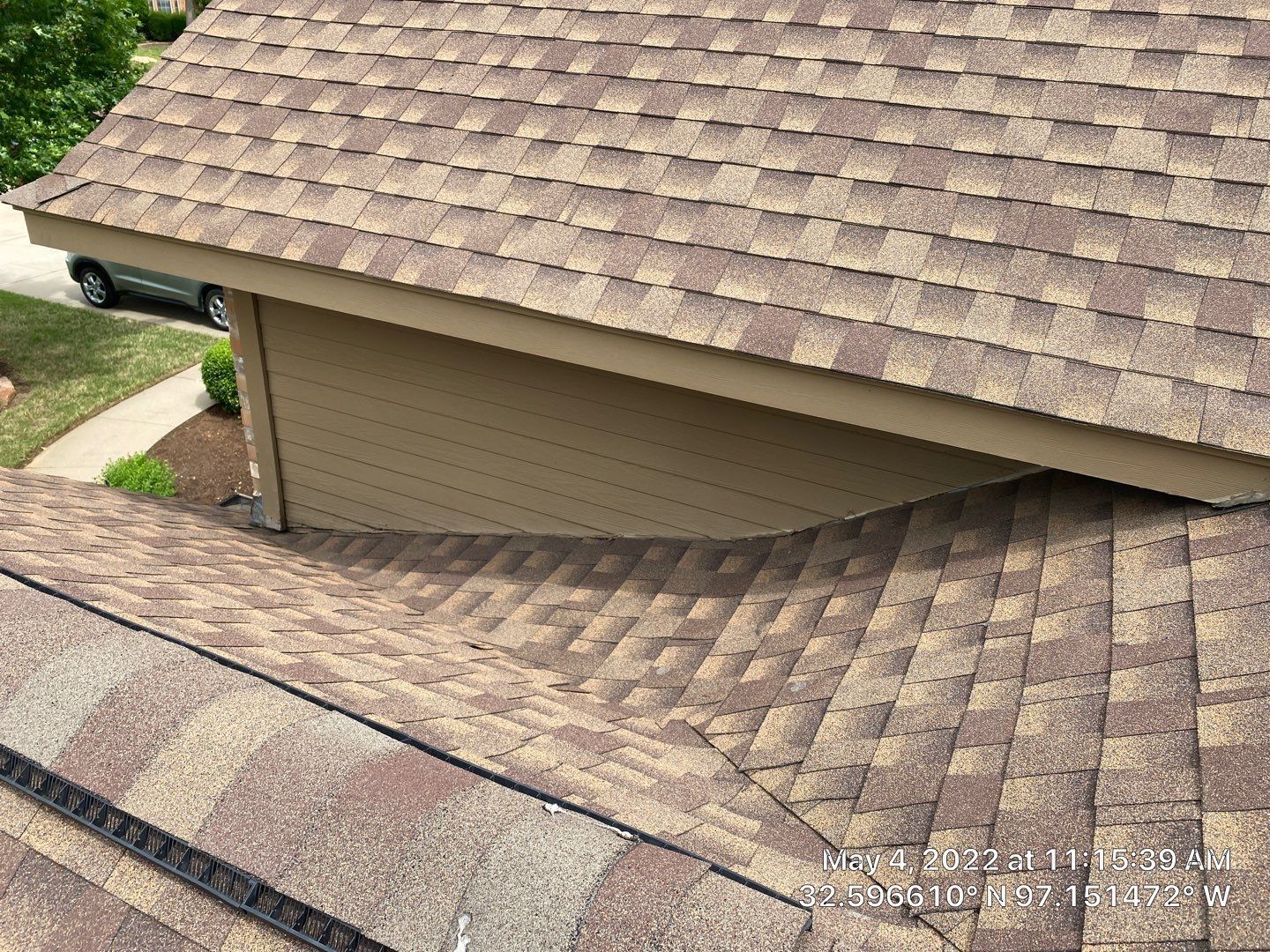Brown asphalt shingle roof, with a secondary roof angled downward towards the right, and a beige wall.