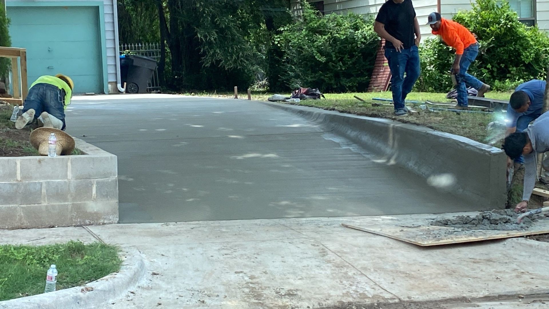 Construction workers pouring concrete for a driveway, with a curb and bordering grass.