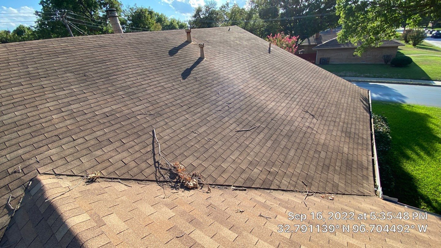 Brown shingled roof with visible damage, vents, and surrounding green lawn.