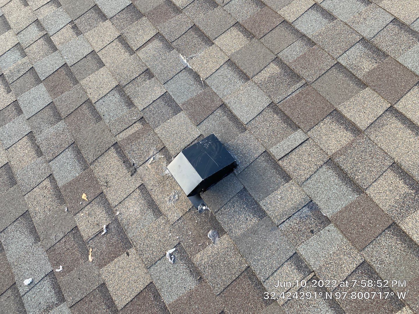 Black and white capped vent on brown and gray asphalt shingle roof.