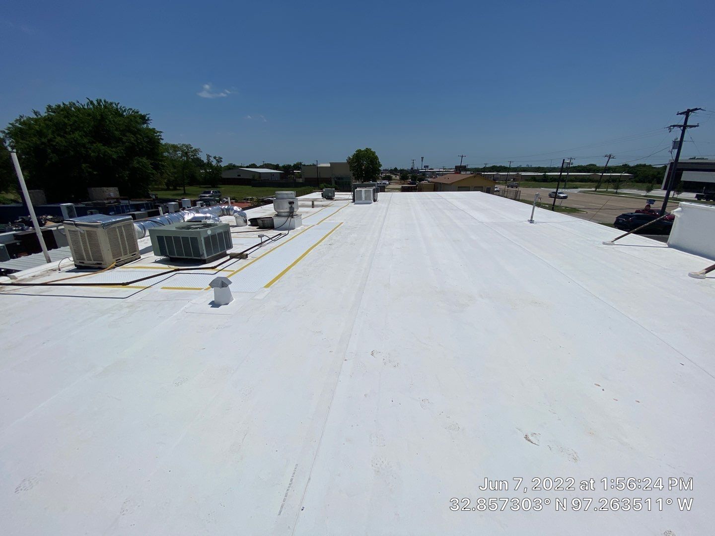 White commercial roof with HVAC units under a clear, blue sky.