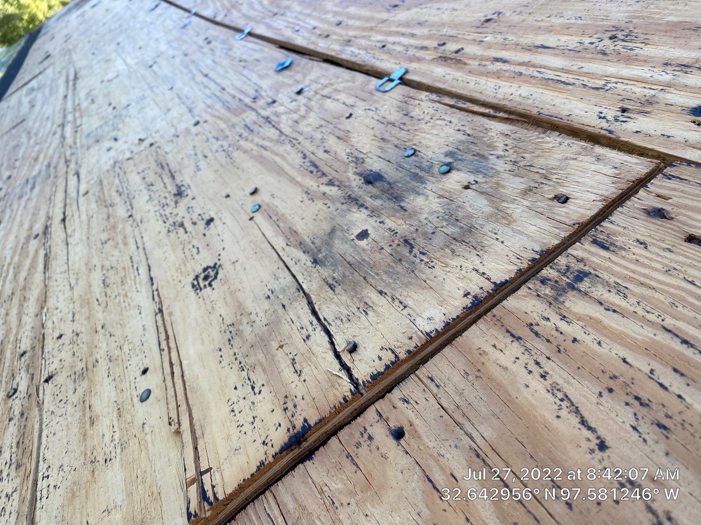 Overhead view of a weathered wooden roof with a cracked, rectangular seam and metal fasteners.