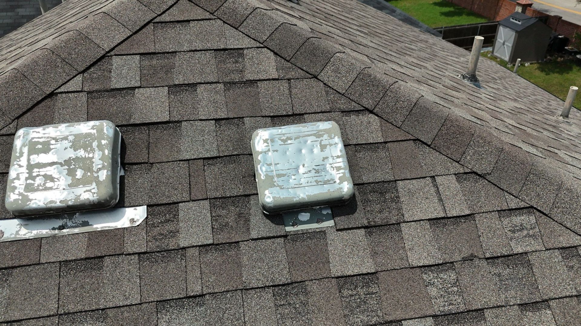 Two weathered metal vent covers on a shingled roof.