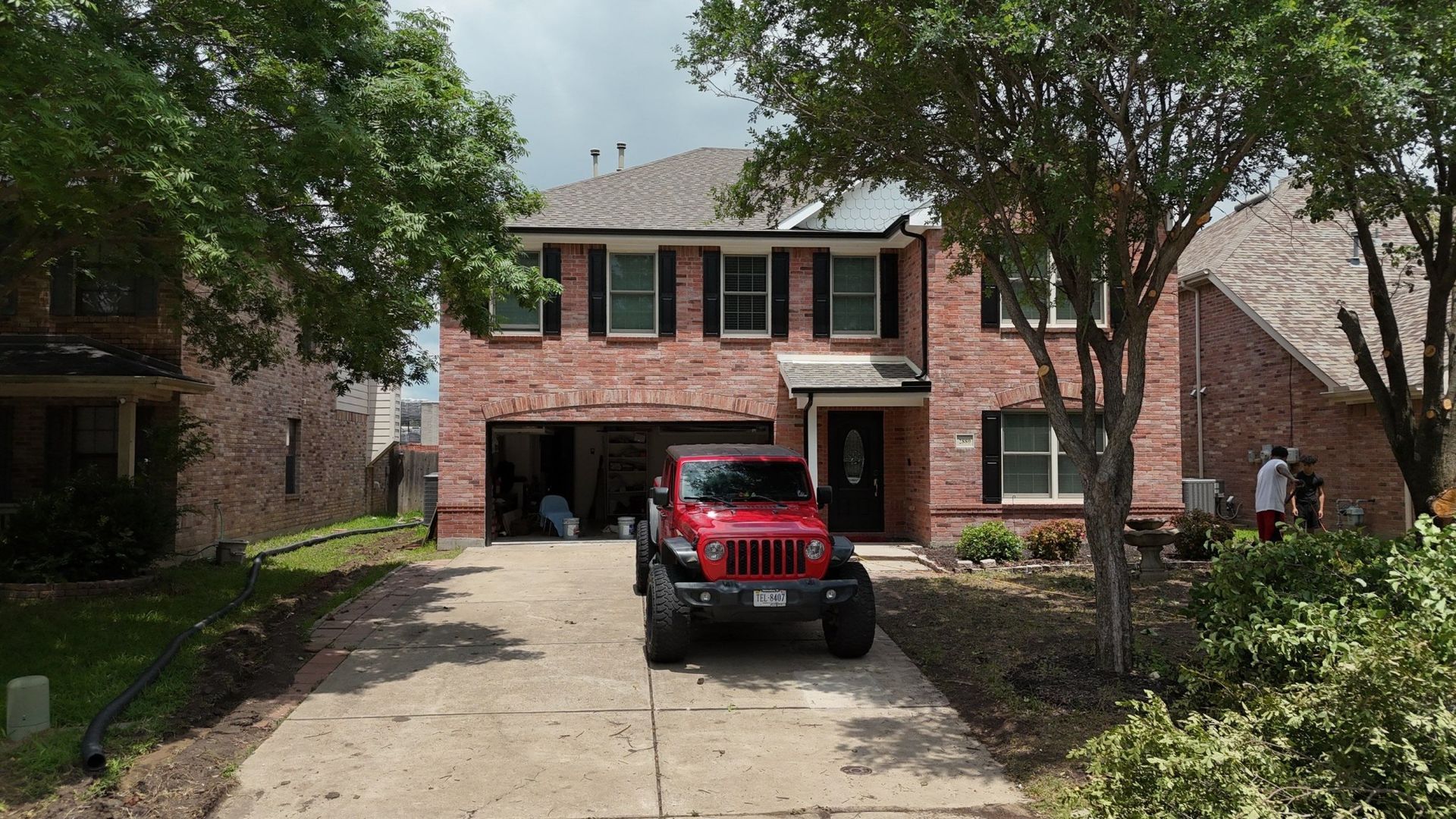 Red Jeep parked in front of a two-story brick house with an open garage.