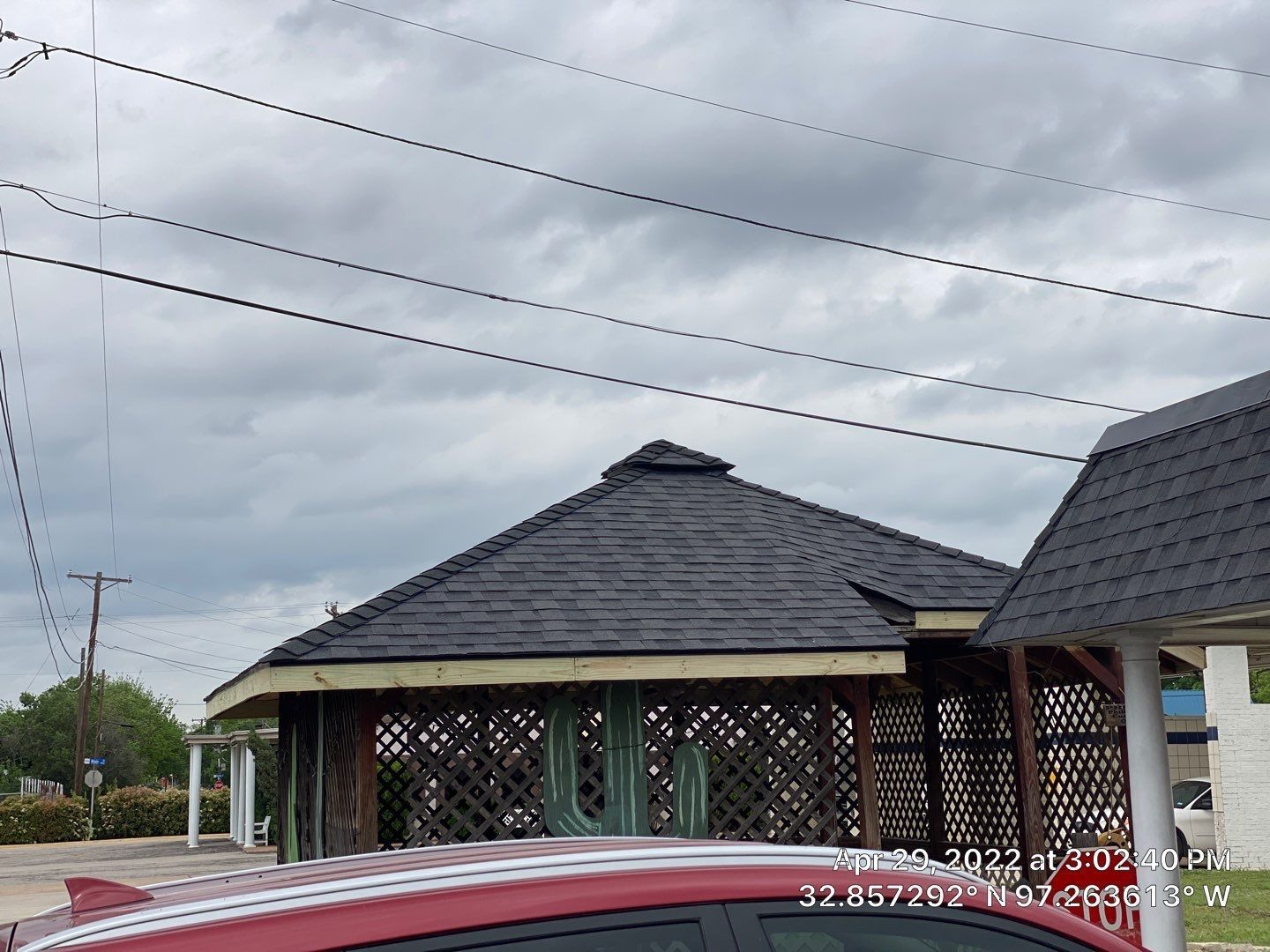 A gazebo with dark shingled roof, latticework walls, and a car in front on a cloudy day.