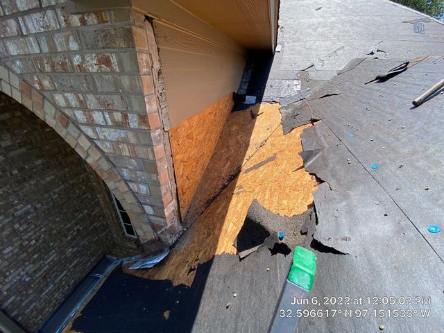 Damaged building: Ruined roof with exposed wooden beams, boarded-up window, white textured wall, and cloudy sky.