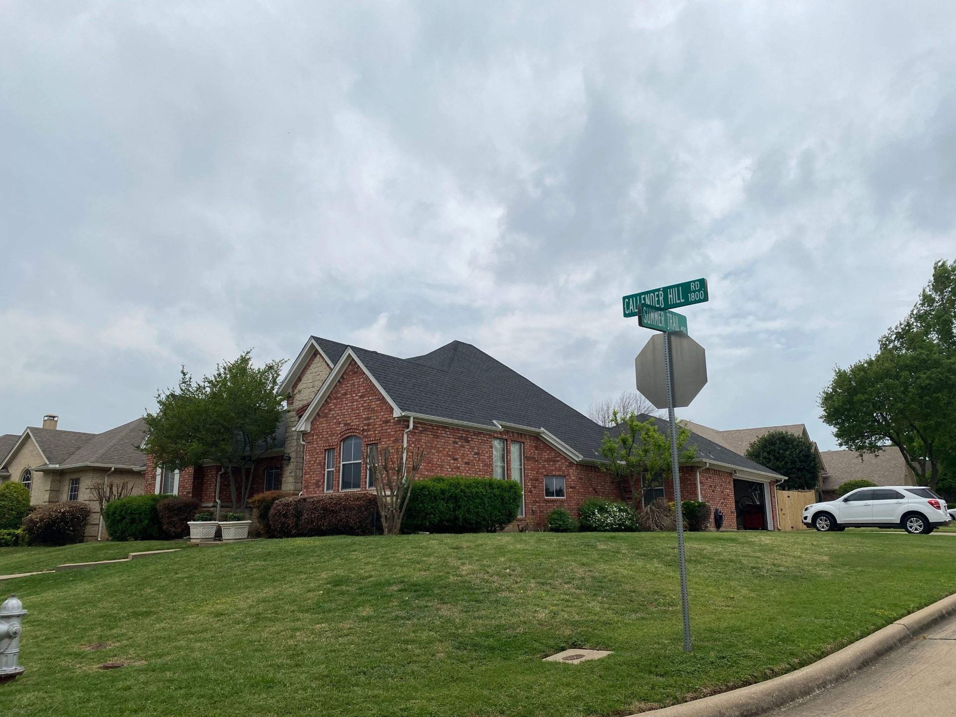 Red brick house on a green lawn with a street sign under a cloudy sky.