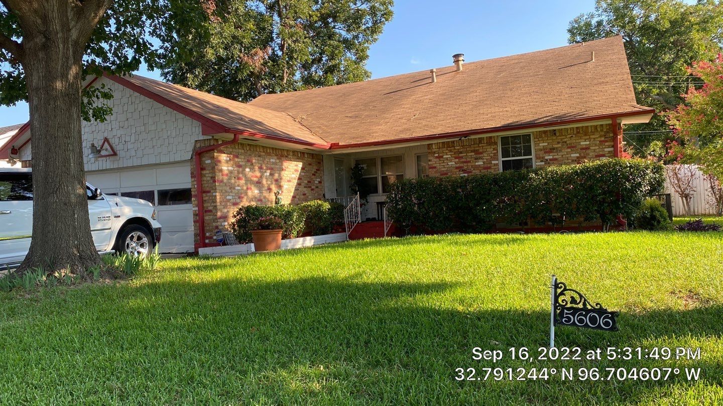 House with brown roof, brick and siding exterior, green lawn, white car parked in garage, blue sky.