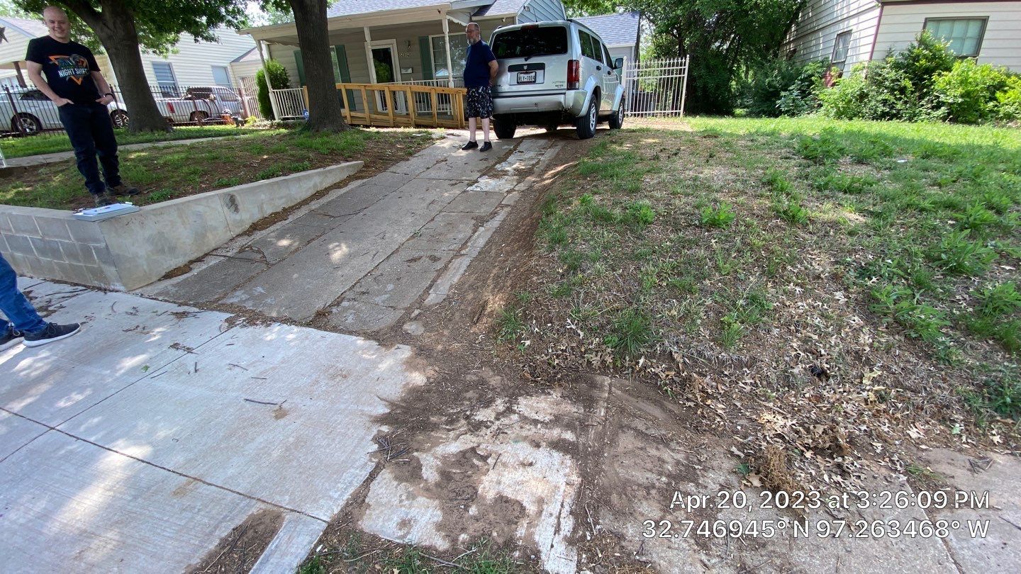 People loading items into a white SUV parked on a sloped driveway next to a house.