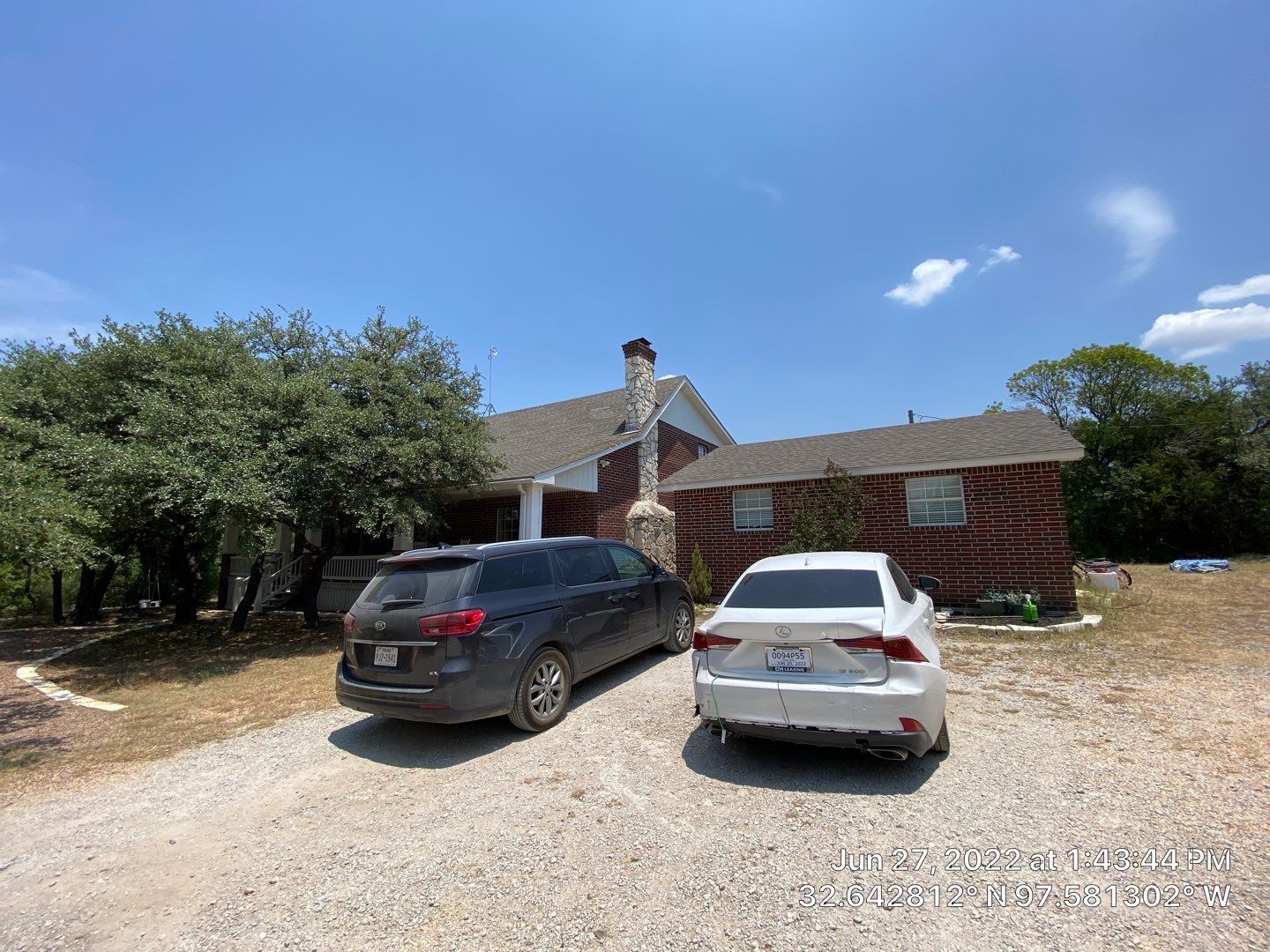 House with two cars parked on a gravel driveway under a blue sky.