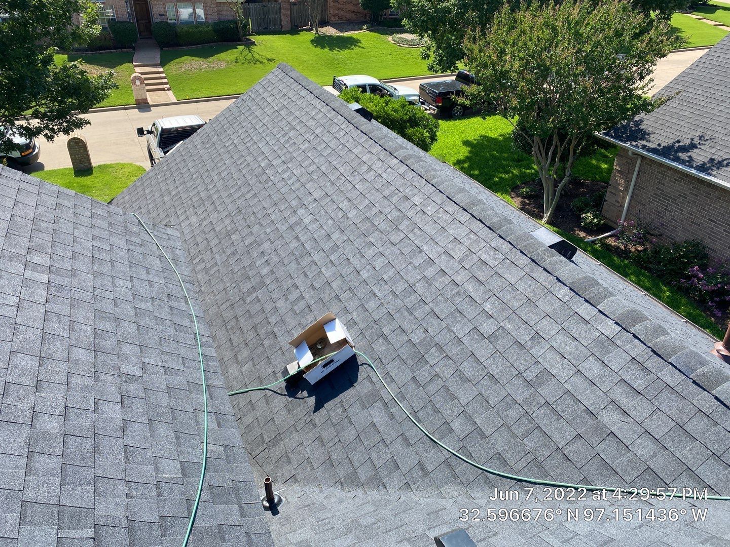 A roof covered in gray shingles, a chimney, and a hose are visible from above.