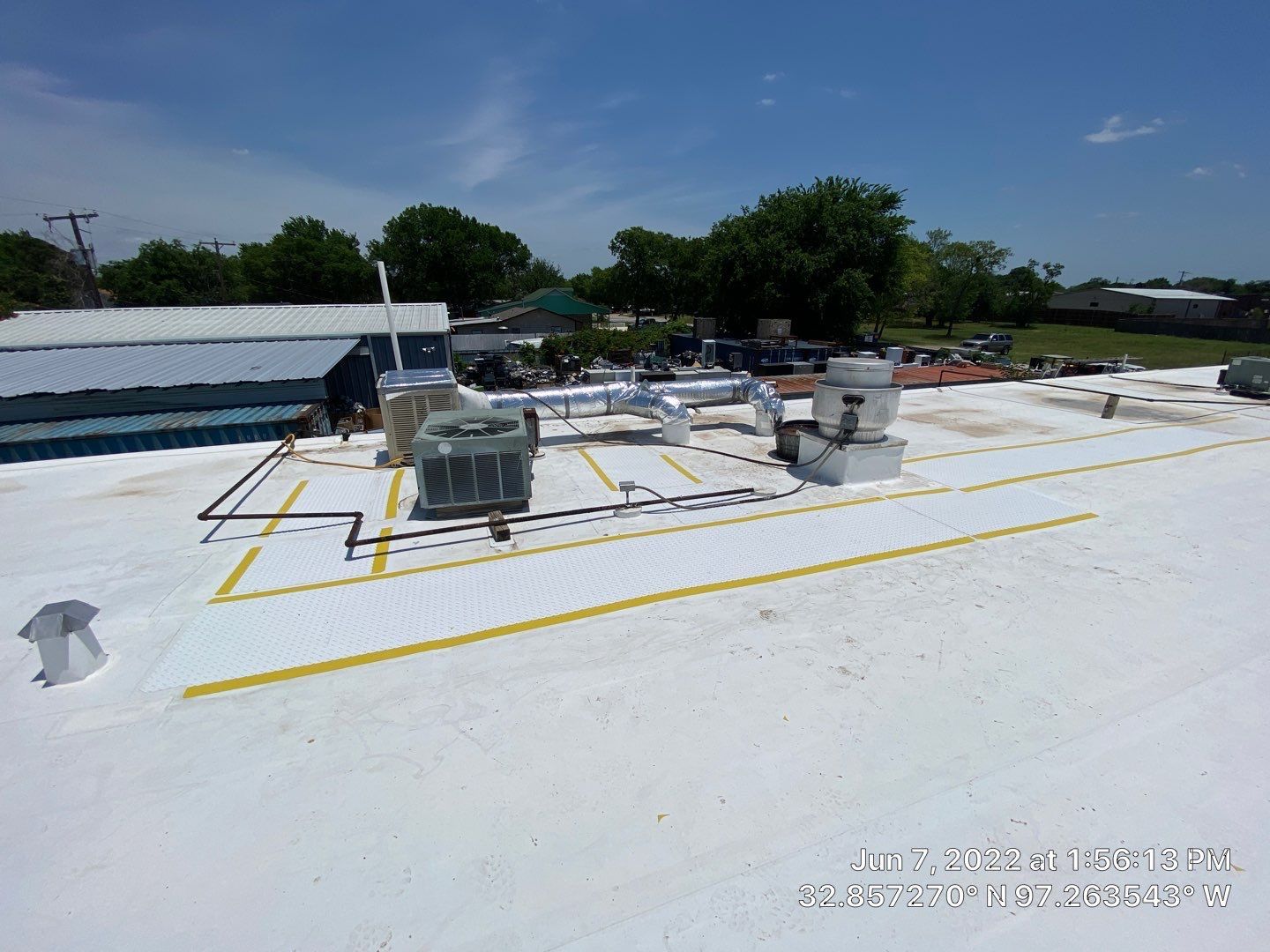 A flat white roof with HVAC units, ductwork, and yellow painted lines against a blue sky.