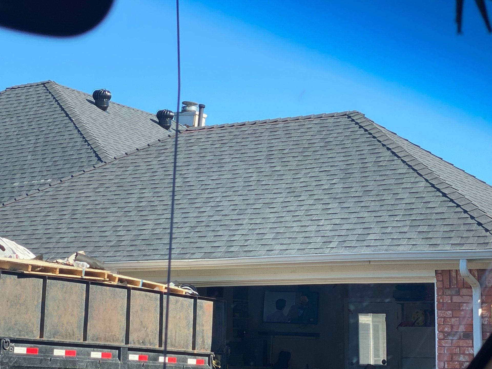 Gray shingled roof with chimneys above a garage. A truck with debris is in the foreground.