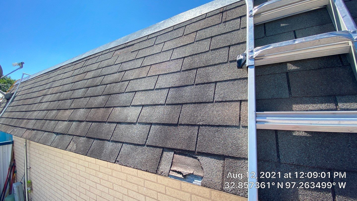 Roof with dark shingles and a metal ladder on a sunny day.