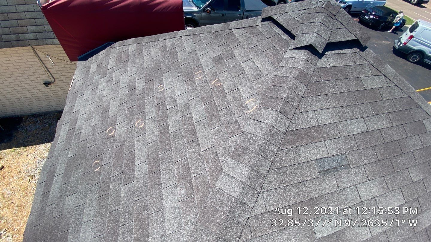 Overhead view of a gray shingle roof on a building. Red object is partially visible on left. Vehicles on the right.