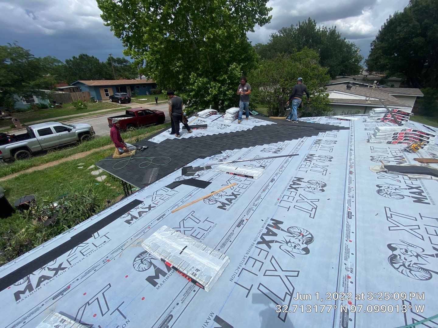 Workers installing roofing shingles on a residential roof, with tools and materials visible.