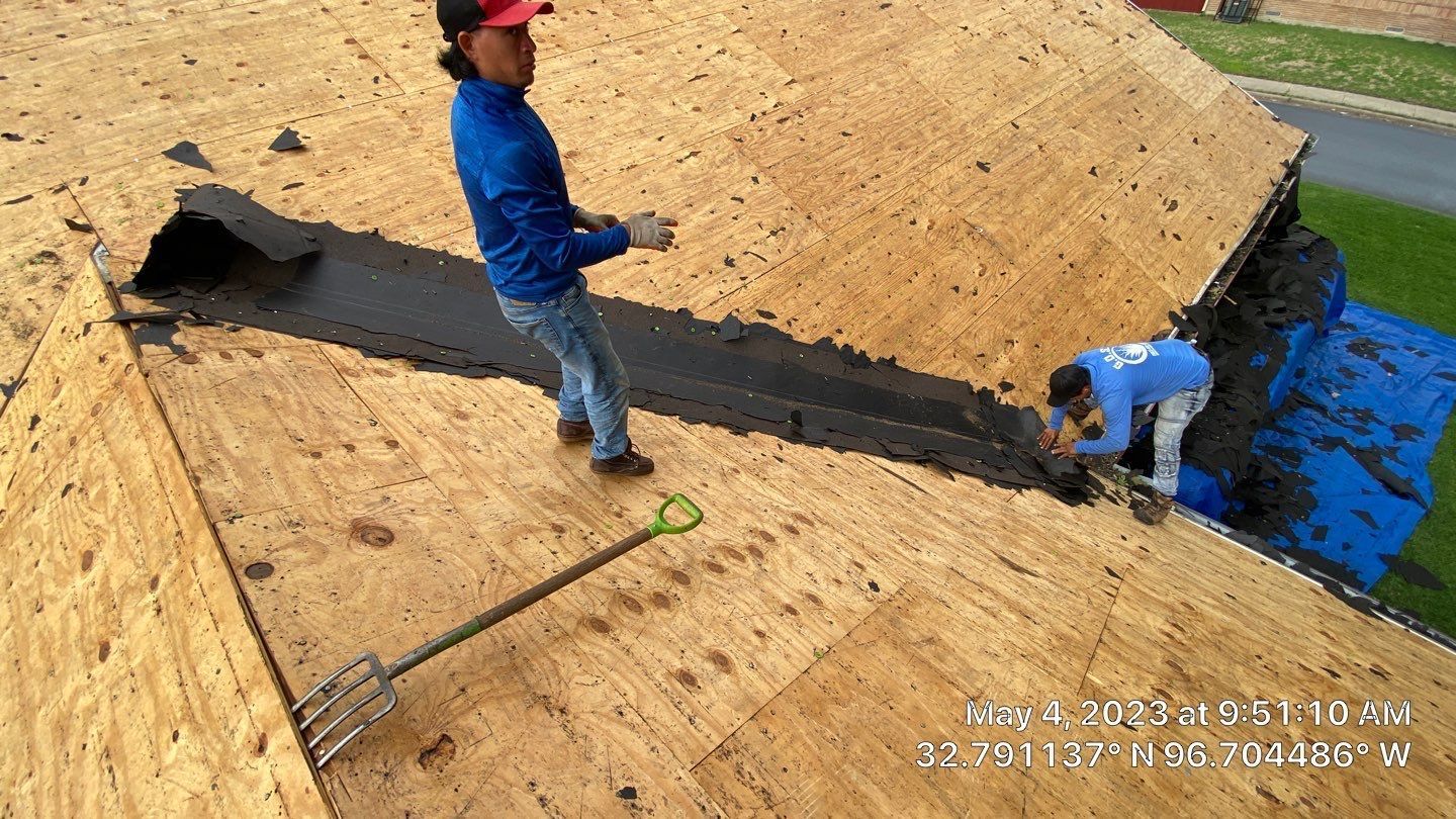 Two people working on a roof, applying a black sealant to the exposed wood. A shovel lays on the wood.