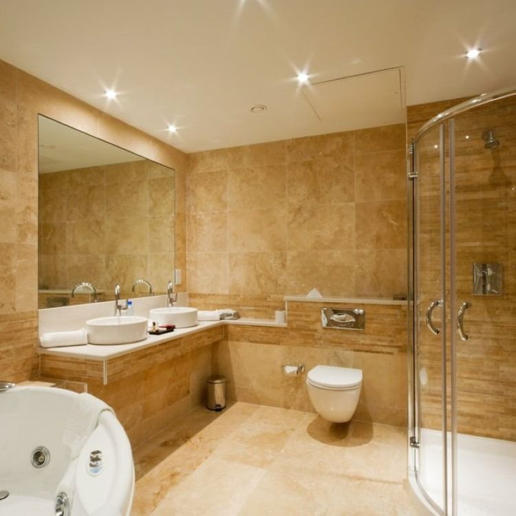 Modern bathroom with beige tile, white fixtures, shower, and jacuzzi.