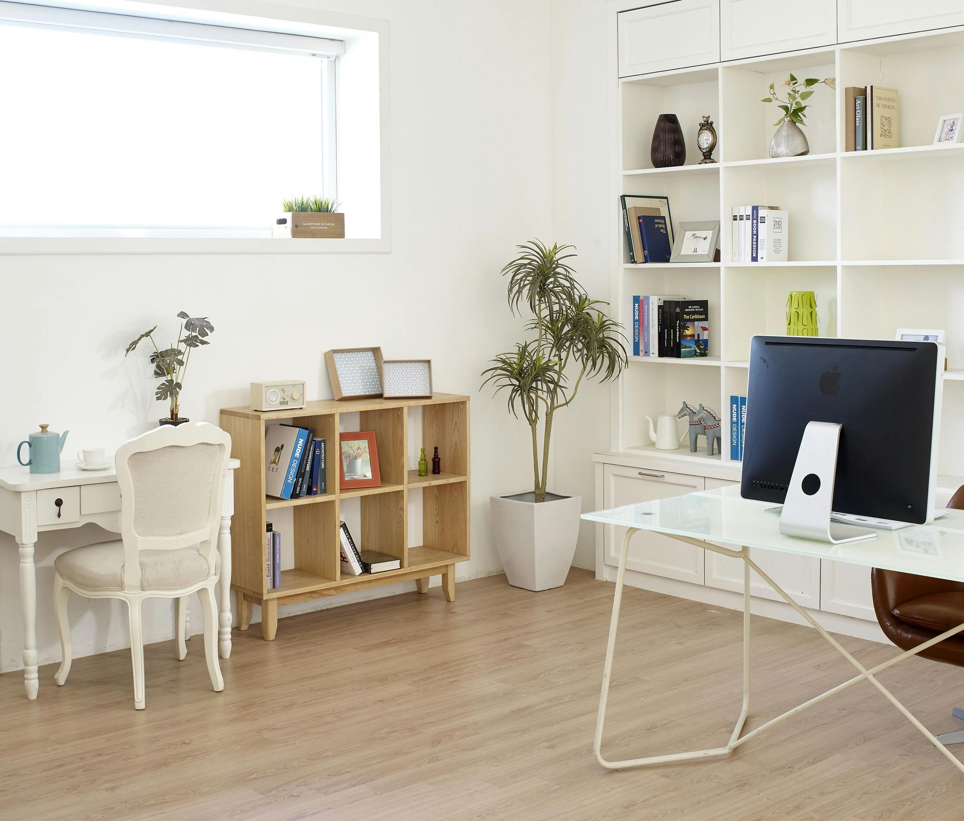 Bright home office with a white desk, chair, and bookshelf filled with decor, and a computer.