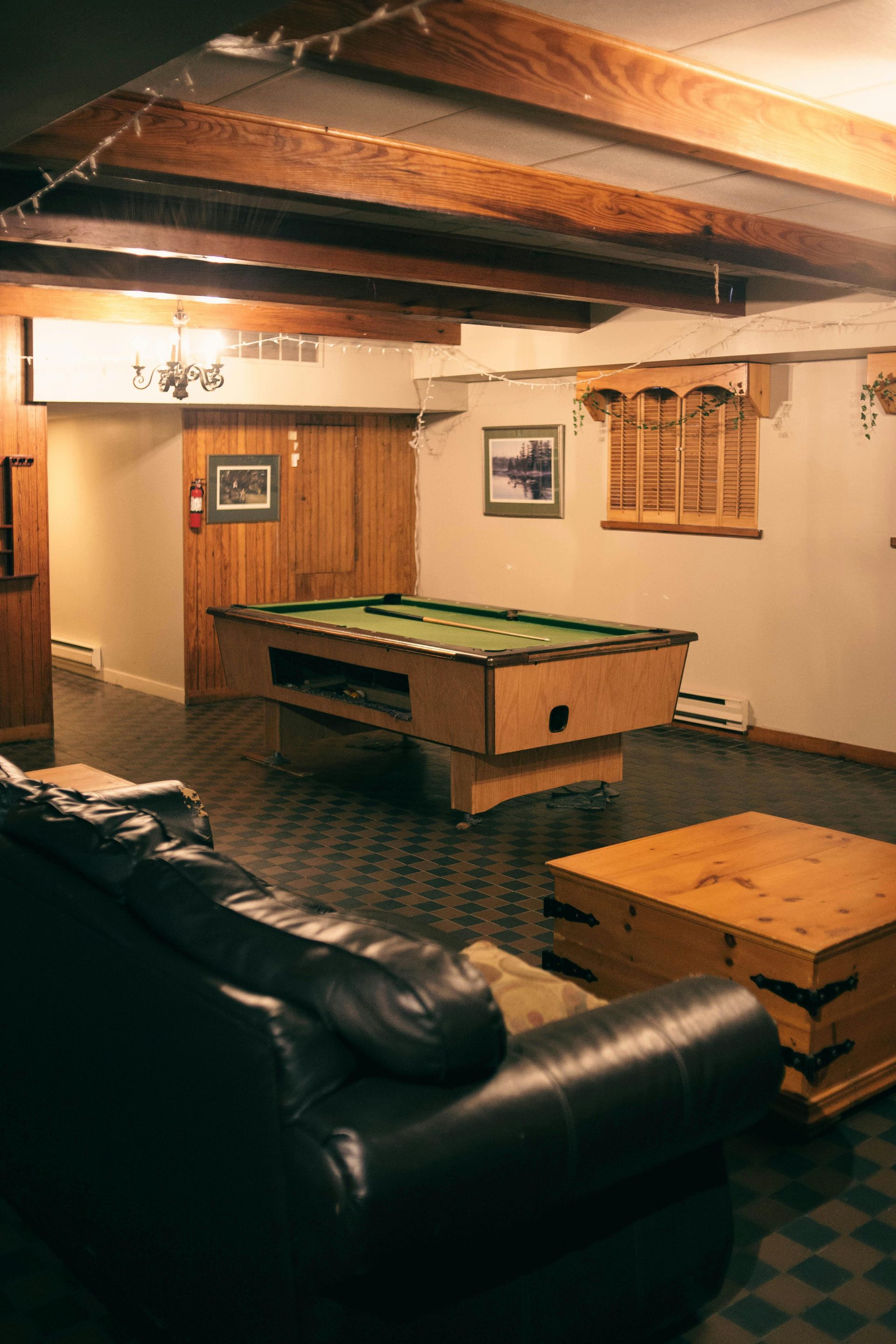 Pool table in a dimly lit basement room with a leather couch and wooden beams.