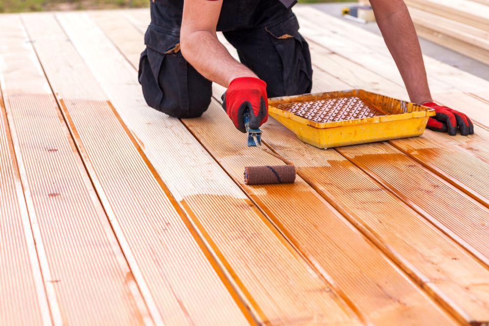 Person applying stain to wooden deck with a roller. Red gloves, yellow tray.